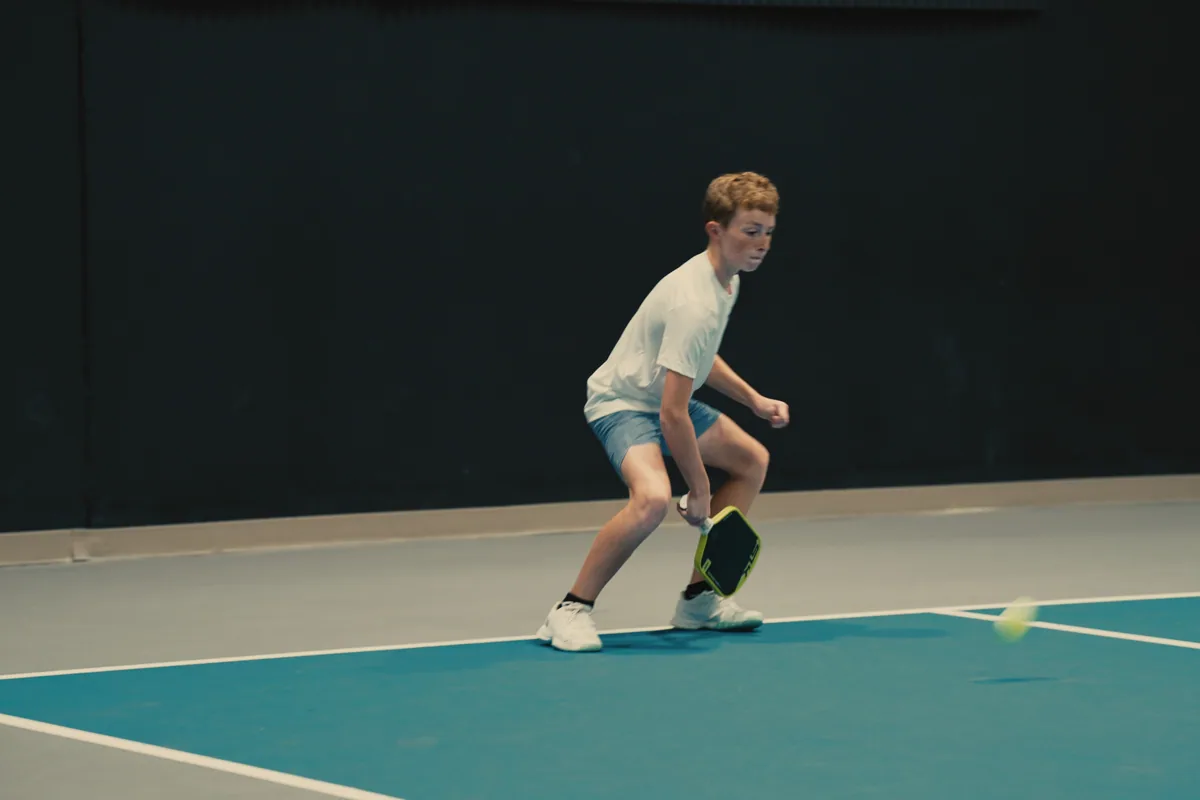 Junior player reading the ball during an indoor pickleball rally.