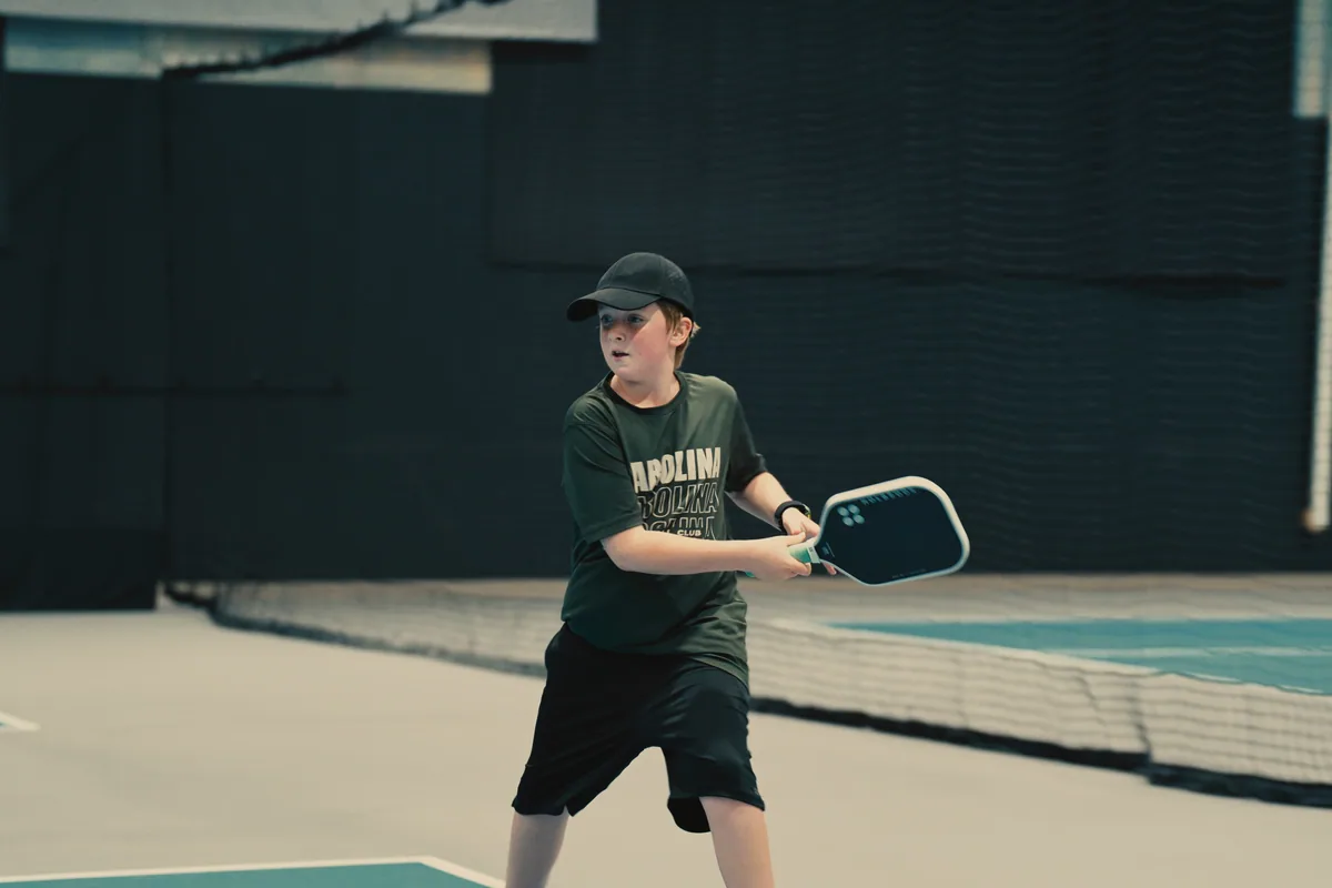Junior player preparing a return on an indoor pickleball court.