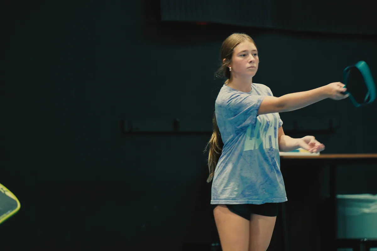 Junior player setting up for a low return on a blue pickleball court.