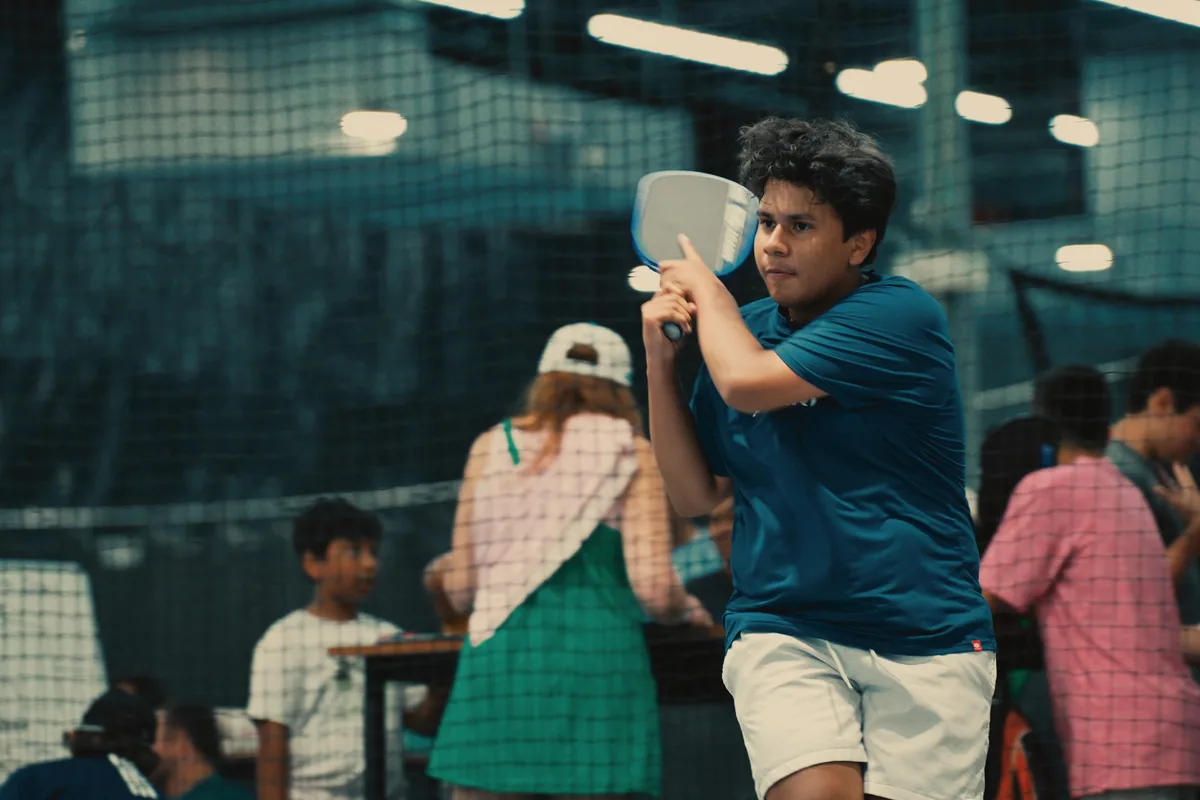 Junior player competing while other players gather on nearby courts.