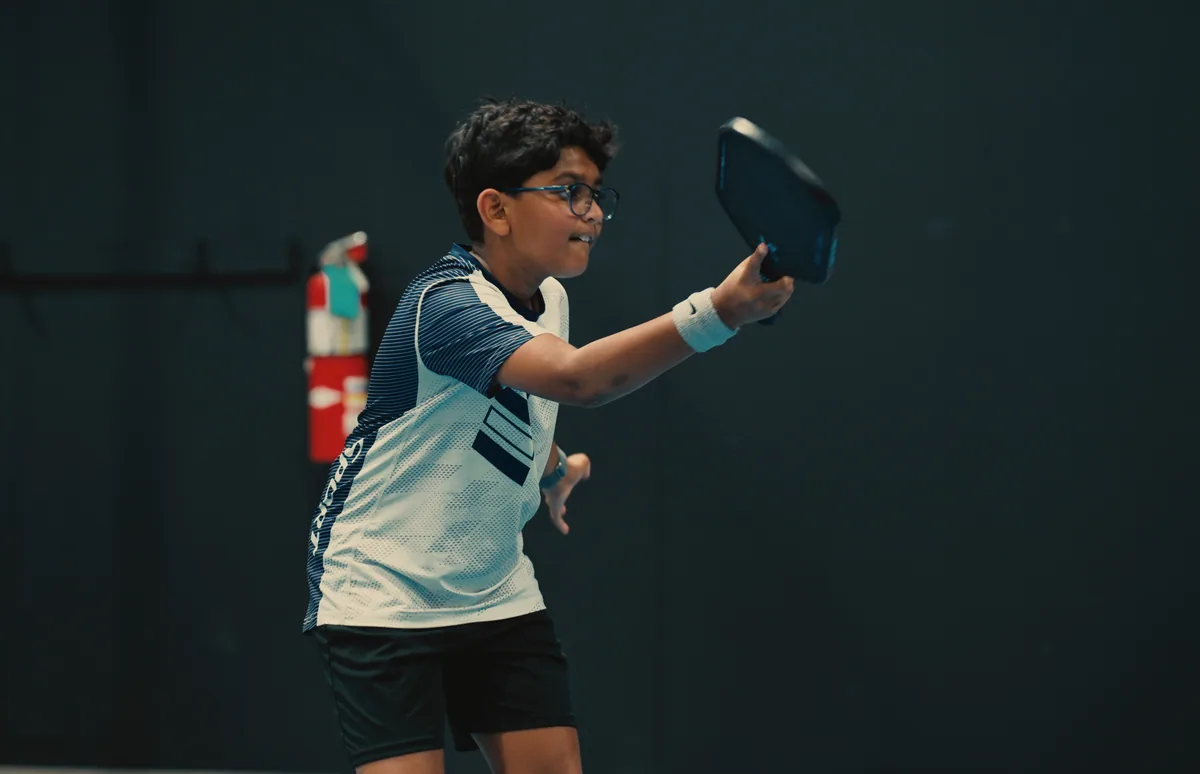 Junior player reaching for a pickleball during focused practice.